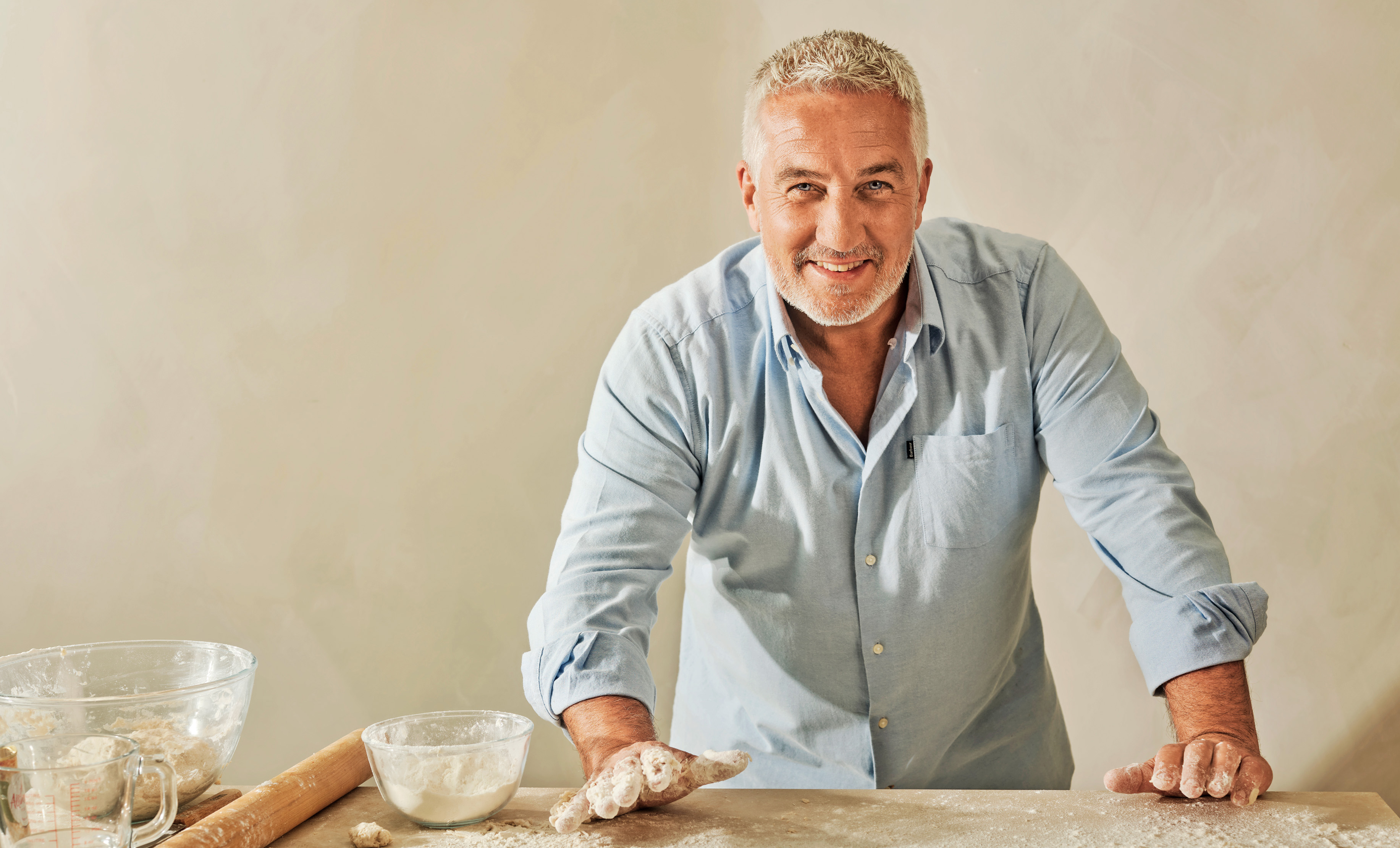 Paul Hollywood with flour on his hands, smiling at the camera.