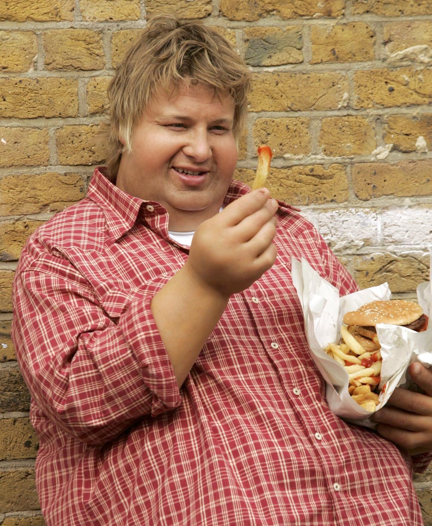 Jamie Oliver in a fat suit eating a burger and chips.