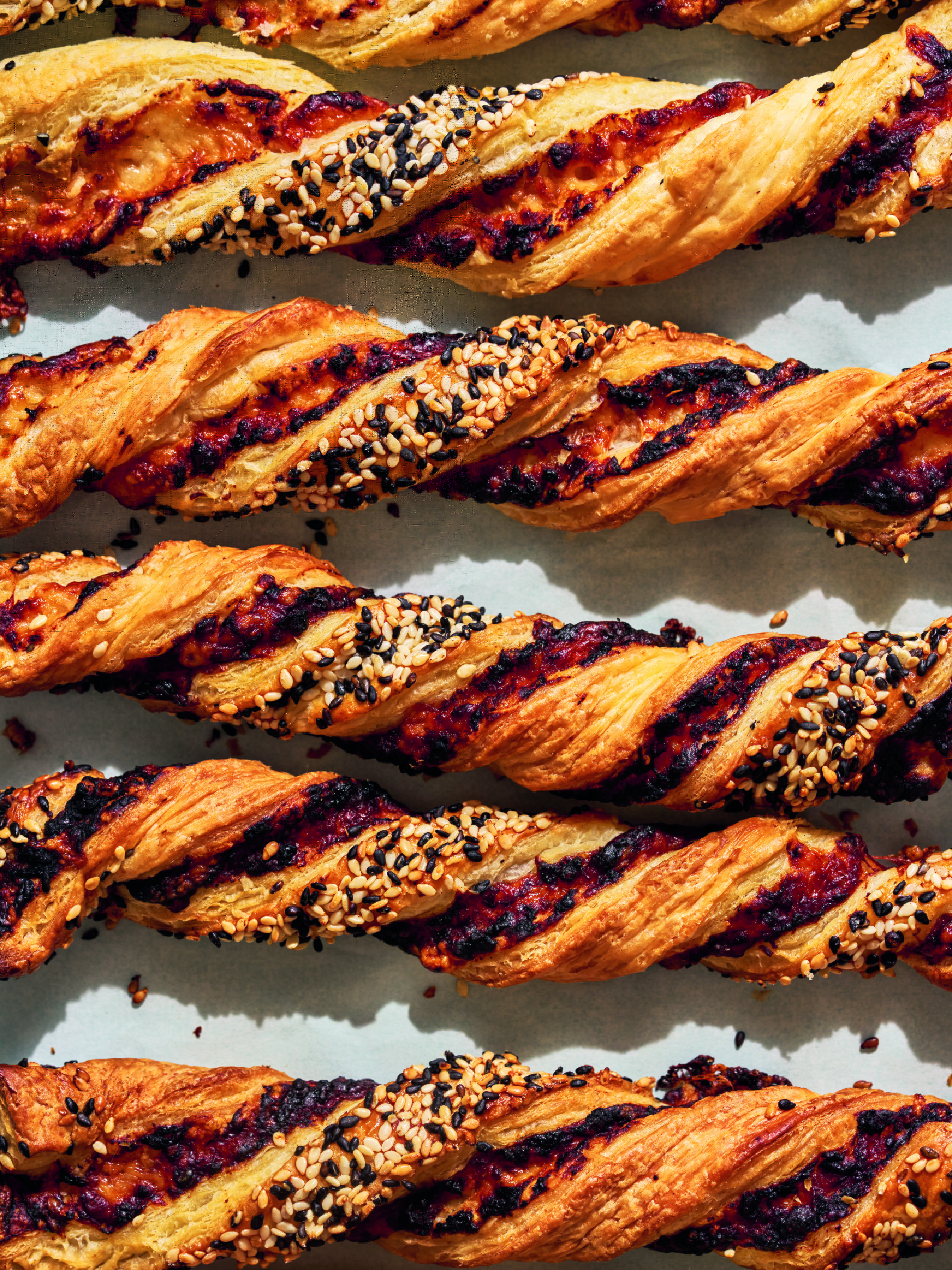 Close-up of several baked pastry twists topped with sesame seeds.